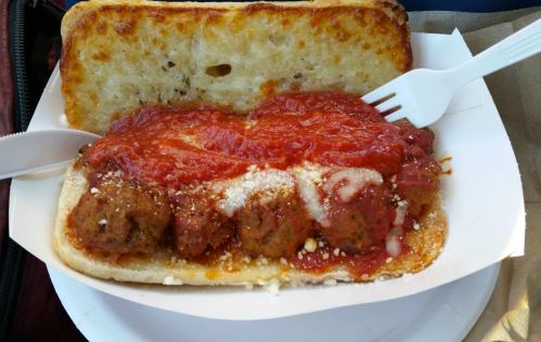 A sandwich with meatballs, marinara sauce, and cheese on a toasted bun, served with a plastic fork.