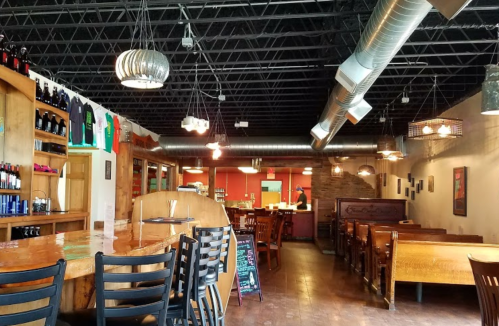 Interior of a restaurant featuring wooden tables, a bar area, and industrial-style lighting.
