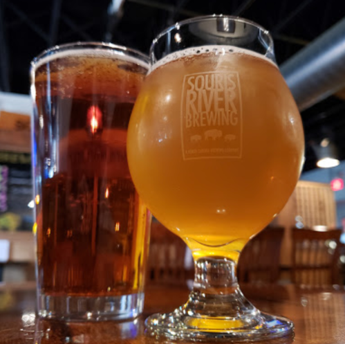 Two glasses of beer on a wooden table: a tall pint of dark beer and a short, round glass of golden beer.