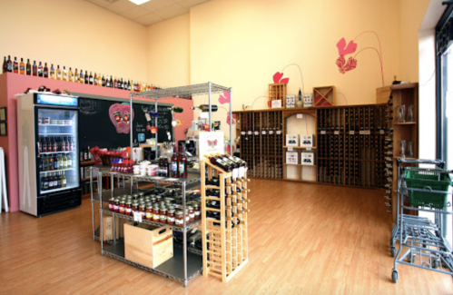 A spacious wine shop with shelves of bottles, a display rack, and a chalkboard, featuring a warm, inviting atmosphere.