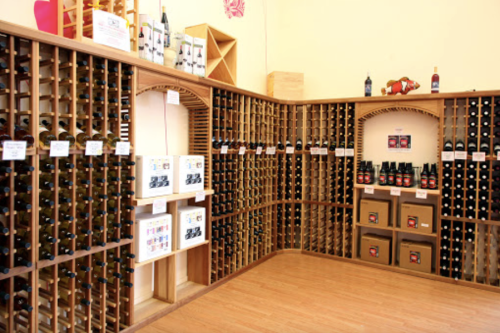 A wine cellar with wooden racks displaying various bottles and boxes of wine on the shelves.
