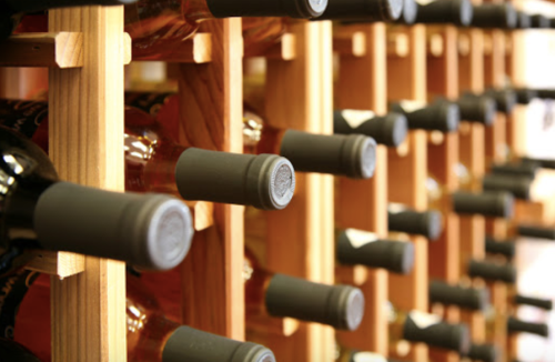 A close-up of wine bottles stored on a wooden rack, showcasing their labels and corked tops.