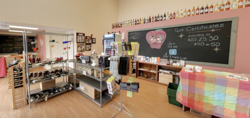 A cozy shop interior featuring shelves of products, a chalkboard, and a colorful display table. Gift certificates available.
