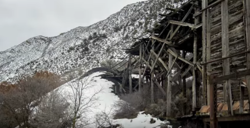 Abandoned wooden structure on a snowy hillside, surrounded by rocky mountains and sparse vegetation.