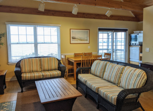 Cozy living area with striped sofas, a wooden coffee table, and a dining table by large windows overlooking a scenic view.