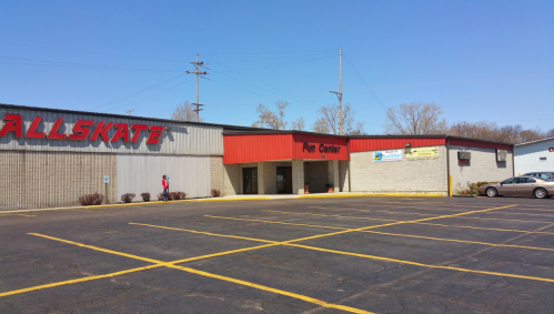 Exterior view of a roller skating rink with a parking lot, clear blue sky, and a few trees in the background.