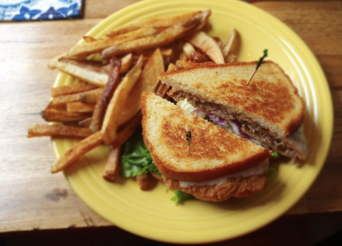 A golden-brown sandwich with lettuce and sliced meat, served with a side of crispy French fries on a yellow plate.