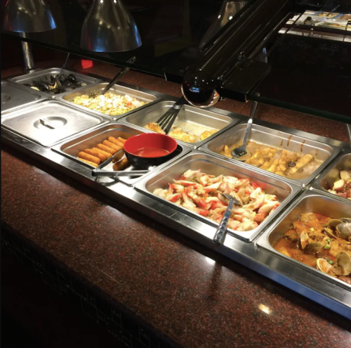 A buffet display featuring various dishes, including seafood, vegetables, and appetizers in metal trays.