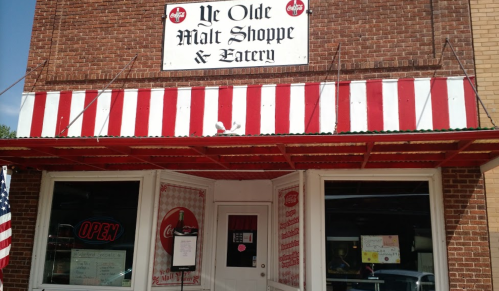 Exterior of Ye Olde Malt Shoppe & Eatery with a red and white striped awning and an "Open" sign in the window.