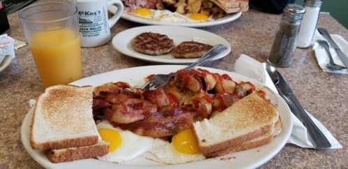 A hearty breakfast plate with eggs, bacon, sausage, and toast, alongside a glass of orange juice.