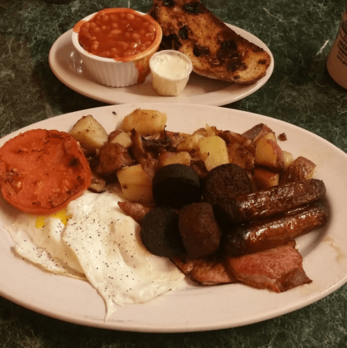 A hearty breakfast plate with eggs, sausage, potatoes, and a slice of tomato, alongside baked beans and toast.
