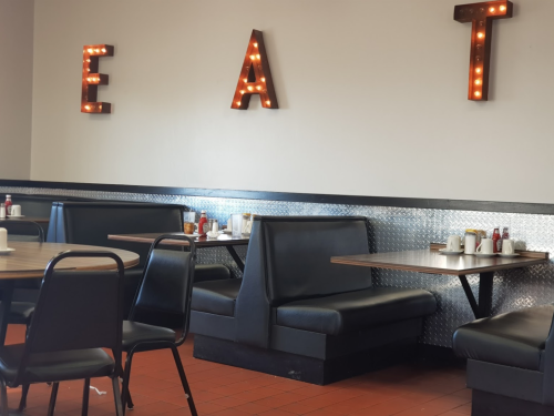 A cozy diner interior with black booths and illuminated letters spelling "EAT" on the wall.