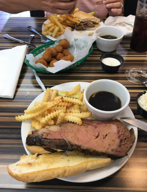 A plate with sliced roast beef, crinkle-cut fries, and dipping sauce, with a side of fried snacks in the background.