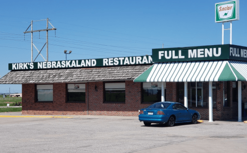 Exterior of Kirk's Nebraskaland Restaurant with a green and white awning and a blue car parked outside.