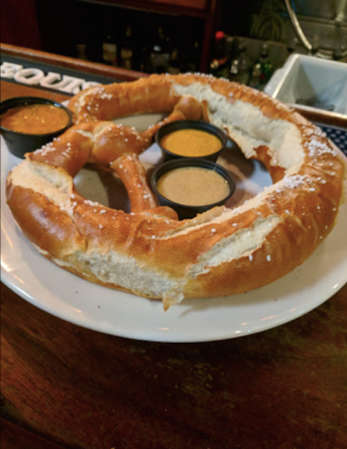 A large pretzel on a plate, served with three dipping sauces in small cups.