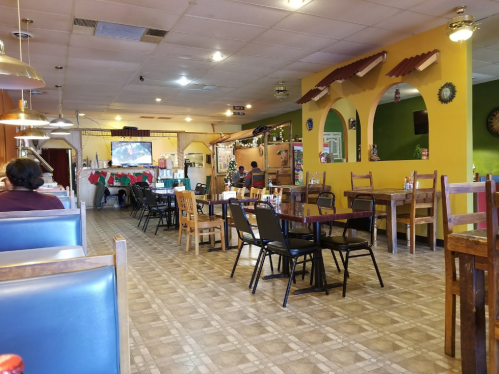 Interior of a restaurant with colorful walls, empty tables, and a TV in the background, decorated for the holidays.