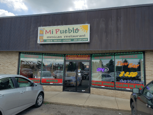 Exterior of Mi Pueblo Mexican Restaurant, featuring a sign and open door, with parked cars in front.
