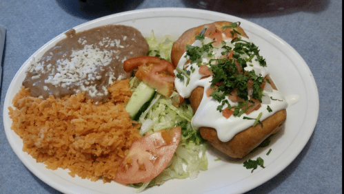A plate of Mexican food featuring two stuffed tortillas, rice, refried beans, lettuce, tomatoes, and sour cream.
