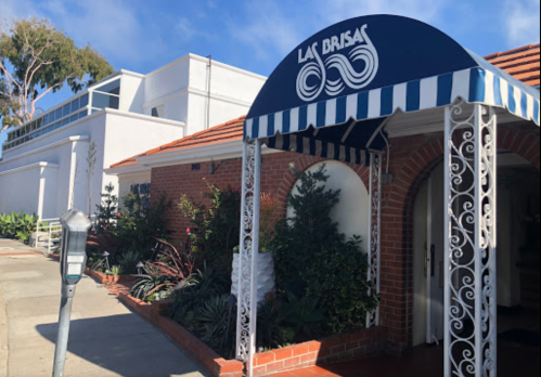 Exterior of Las Brisas restaurant featuring a blue awning, brick facade, and lush greenery along the entrance.