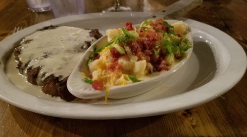 A plate featuring a steak with creamy sauce and a side of macaroni topped with bacon and green onions.