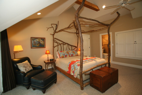 Cozy bedroom featuring a unique branch canopy bed, armchair, and warm lighting in a rustic setting.