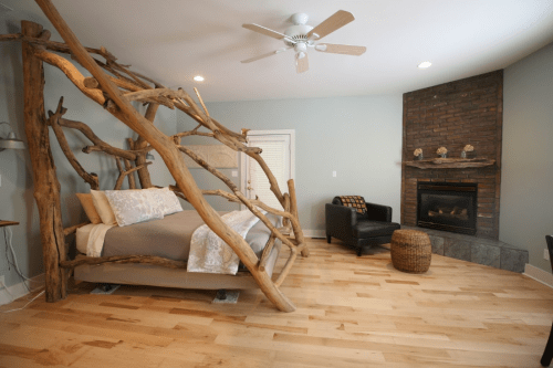 A unique bedroom featuring a wooden bed frame, a cozy fireplace, and light wood flooring.