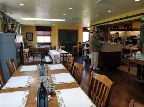 A cozy restaurant interior with wooden tables, a bar area, and two staff members preparing food.