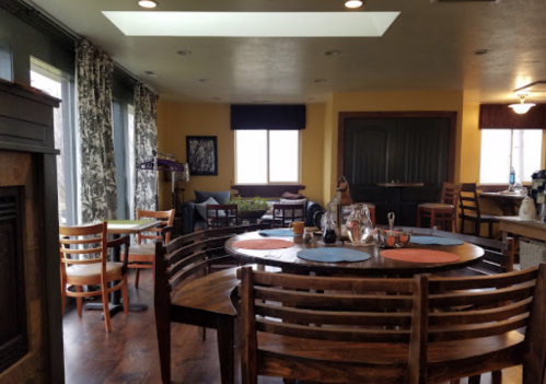 Cozy dining area with wooden tables, colorful chairs, and large windows, featuring a warm, inviting atmosphere.
