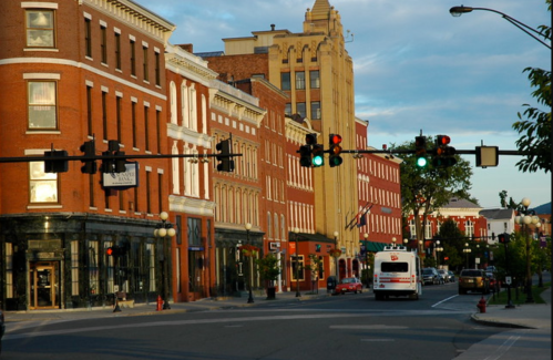 A street view of a historic downtown area with red brick buildings, traffic lights, and a bus on the road.