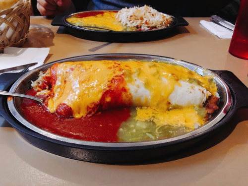 A large burrito topped with melted cheese and sauce, served on a sizzling plate with a side of rice.