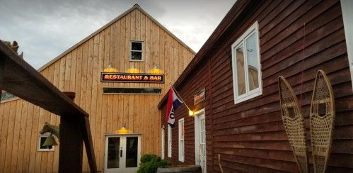 Exterior view of a rustic restaurant and bar with wooden siding and a flag, featuring snowshoes on the wall.