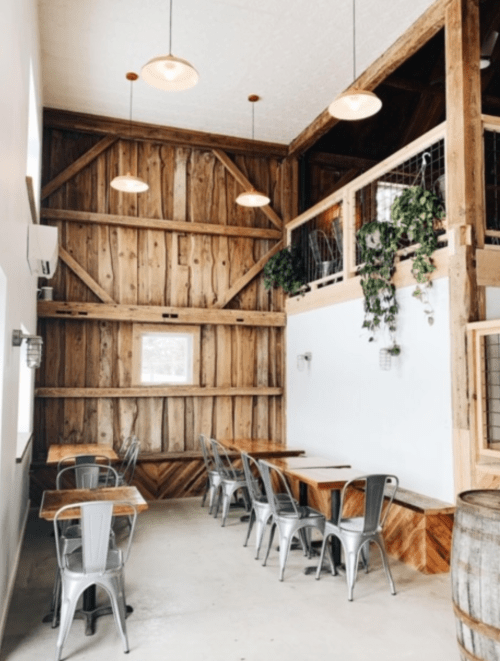 Cozy restaurant interior with wooden walls, metal tables, and hanging plants, featuring warm lighting and a rustic vibe.