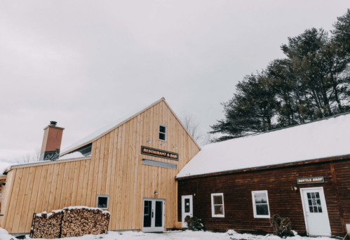 A snowy scene featuring a wooden restaurant and bar building alongside a bottle shop.