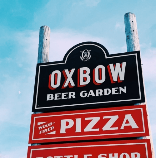 Sign for Oxbow Beer Garden featuring wood-fired pizza and a bottle shop, set against a blue sky.