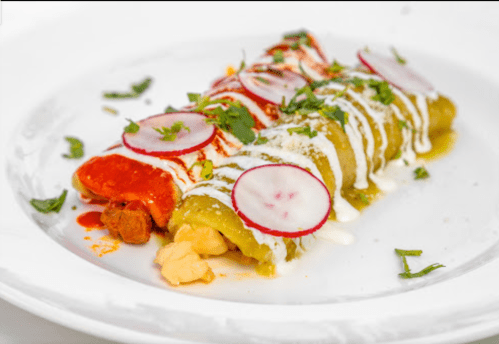 A plate of colorful enchiladas topped with radishes, cilantro, and drizzled with sauce.