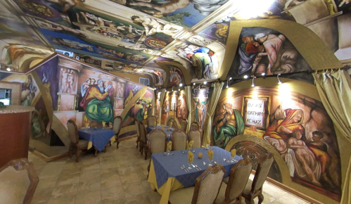 A beautifully decorated restaurant with intricate ceiling and wall murals, featuring elegant tables set for dining.