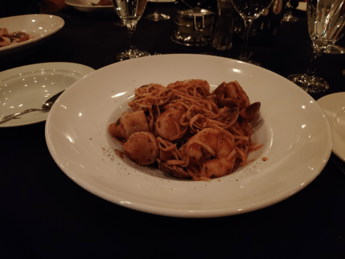 A plate of pasta with seafood, including shrimp and scallops, served on a white dish with elegant table settings.