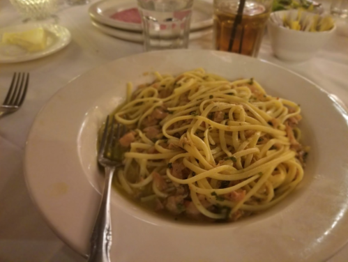 A plate of pasta with a light sauce, garnished with herbs, served on a white dish with a fork beside it.