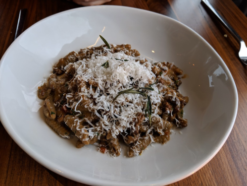 A bowl of pasta topped with grated cheese and herbs, served on a wooden table.