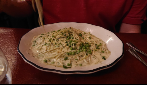 A plate of creamy pasta with peas, garnished with herbs, on a table with utensils and a glass of water nearby.