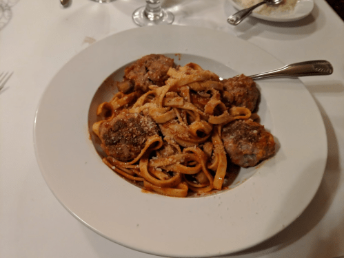 A plate of fettuccine pasta topped with meatballs and grated cheese, served on a white tablecloth.