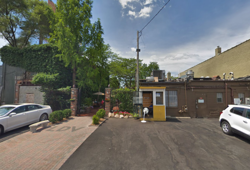 A narrow alleyway with parked cars, greenery, and a small building with a yellow door under a blue sky.