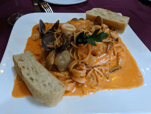 A plate of seafood pasta in a creamy sauce, garnished with parsley, accompanied by two slices of bread.