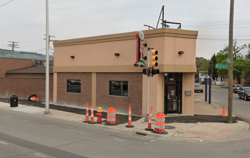 A corner building with a sign, surrounded by traffic cones and construction barriers, on a city street.