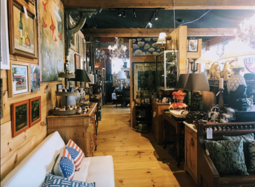 A cozy antique shop interior with wooden floors, various artworks, and vintage furniture displayed throughout.