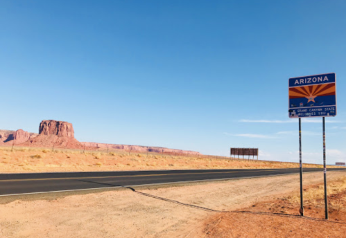 A road sign marking the entrance to Arizona, with a desert landscape and rock formations in the background.