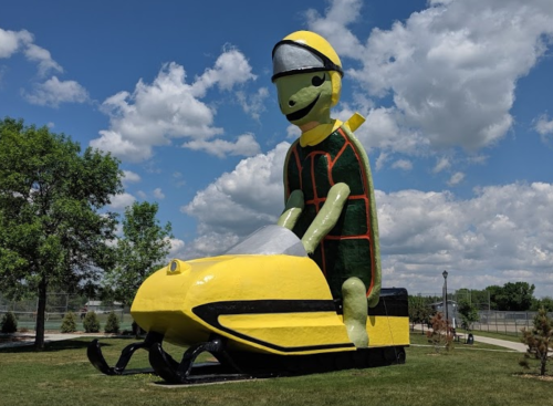 A large, colorful statue of a person in a yellow helmet riding a yellow snowmobile against a cloudy sky.