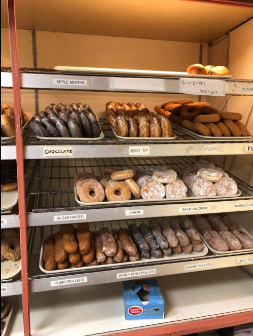 A display of assorted donuts and muffins on shelves, including chocolate, honey dip, and apple muffins.