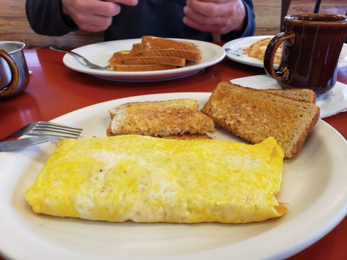 A plate with a fluffy omelet, two slices of toast, and a cup of coffee on a red table.