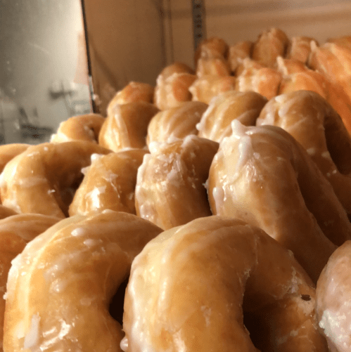 A close-up of glazed donuts stacked in a display case, showcasing their shiny, golden-brown surface.